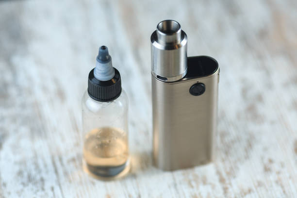 istock Silver electronic cigarette mod and a jar with fluid with nikotine stand on the table. 642708348