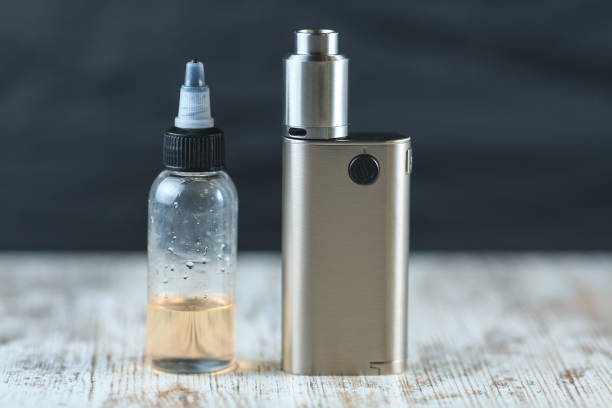 Silver electronic cigarette mod and a jar with fluid with nikotine stand on the table.