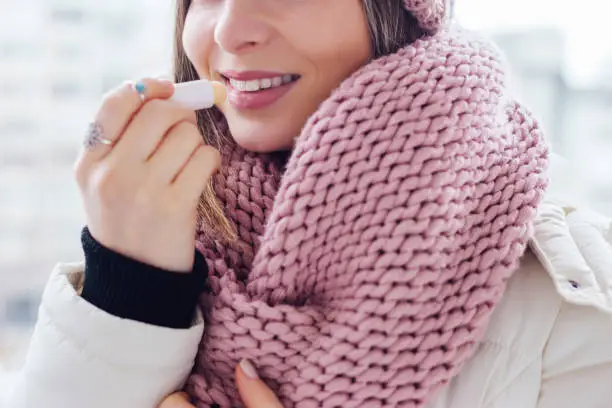 Young women apply lip care balm outside, on cold weather