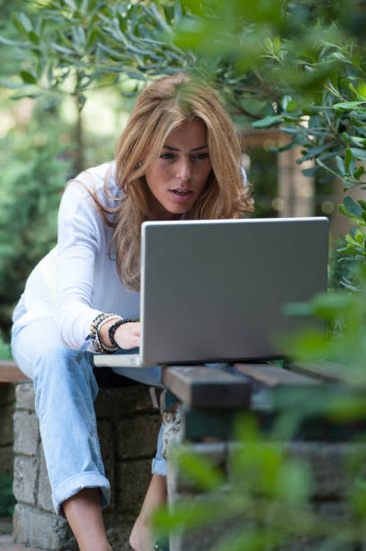 istock Beautiful Woman Using Laptop While Sitting On Bench At Park 642784784