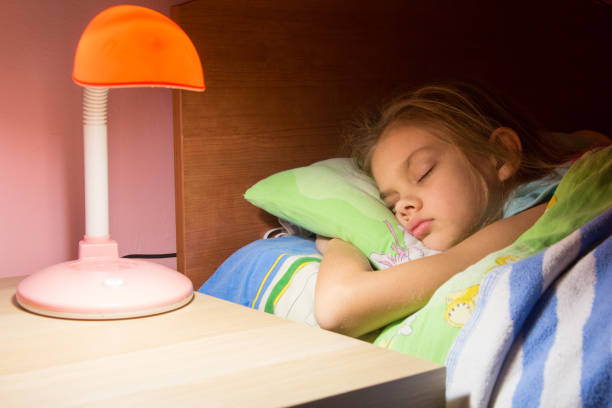 ragazza di sette anni addormentata a letto, la lampada da lettura è inclusa sul tavolo successivo - comodino foto e immagini stock