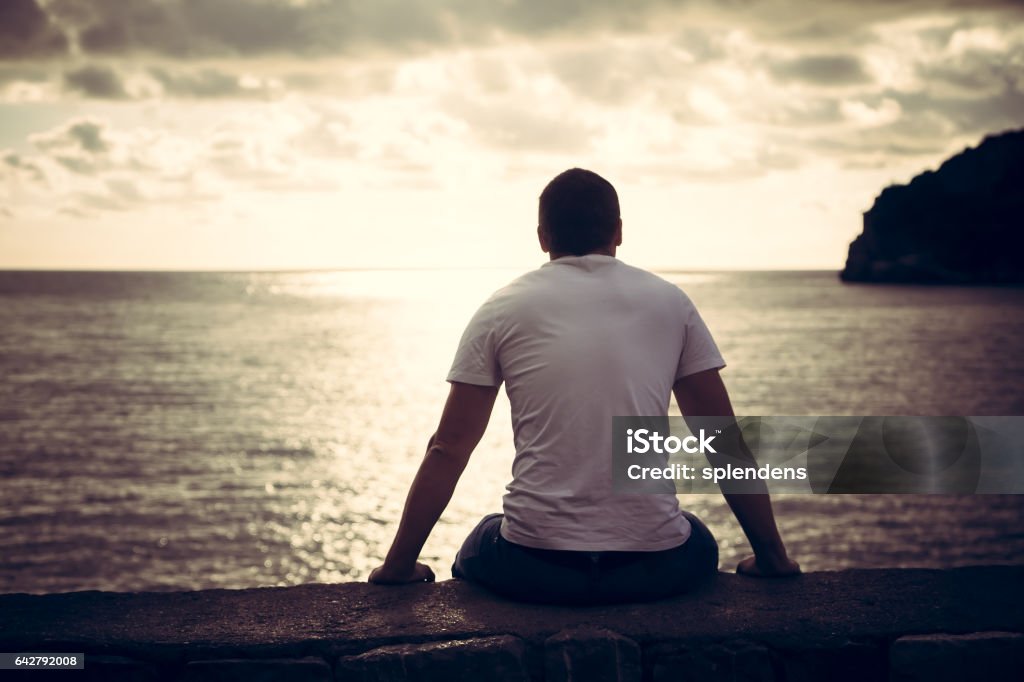 Lonely man looking with hope at horizon with sunlight during sunset with effect of light at the end of tunnel Rear view of lonely man looking with hope at horizon with sunlight during sunset with effect of light at the end of tunnel Men Stock Photo