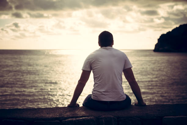 lonely man looking with hope at horizon with sunlight during sunset with effect of light at the end of tunnel - men beach back rear view imagens e fotografias de stock