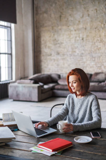 giovane donna che lavora in un appartamento loft con un computer portatile - home interior young adult professional occupation vertical foto e immagini stock