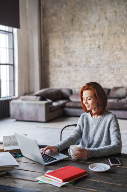 Young woman working in a loft apartment with a laptop computer Young woman using laptop in a loft apartment dyed red hair photos stock pictures, royalty-free photos & images