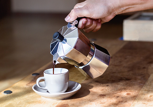 Woman's hand holding coffee maker while pouring coffee on cup