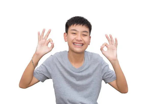 Youngman smiling with teeth brace dental and OK hand sign on isolated background.