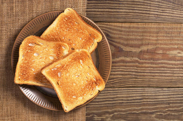 Slices of toasted bread Slices of toasted bread in plate on wooden table, top view. Space for text toasted bread stock pictures, royalty-free photos & images