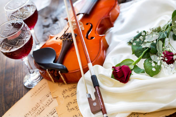 Violin, red rose, wine and music notes on satin fabric stock photo