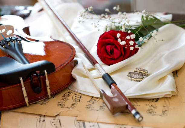 Violin, red rose, marriage rings, wine and music notes on satin fabric stock photo