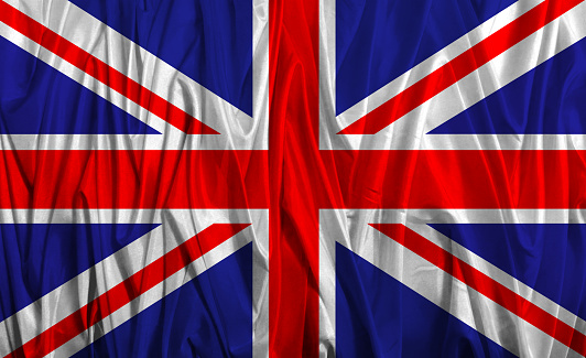 Closeup of a national UK flag with flagpole, blowing in the wind on a blue sky with clouds and copy space. Union Jack Flag.