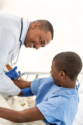 african descent teenage boy being vaccinated by a male doctor