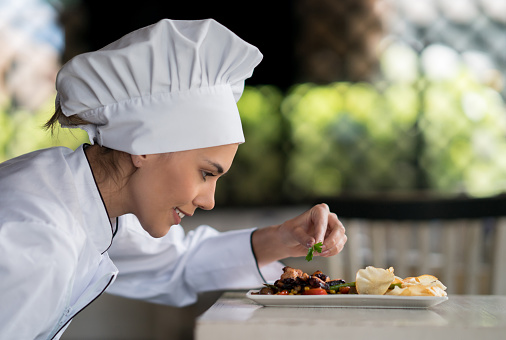 Portrait of a female chef decorating a plate at a restaurant - food and drinks concepts