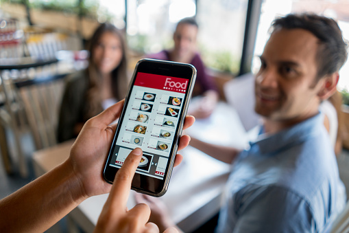 Waitress holding online menu on smart phone at a restaurant - small business using technology. *Design on screen was made from scratch by us.*