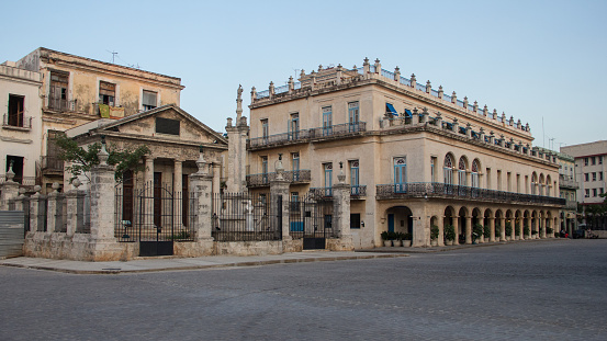 Beautiful old buildings, with columns and arches,  that surround the Plaza de Armas (Armas square) in the Old Havana. The sky has no clouds.