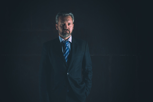 Portrait of a mature businessman in a black suit on dark background