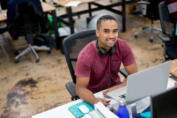 Casual business man working at the office Casual business man working online at the office using a laptop computer and looking at the camera smiling young graphic designer stock pictures, royalty-free photos & images