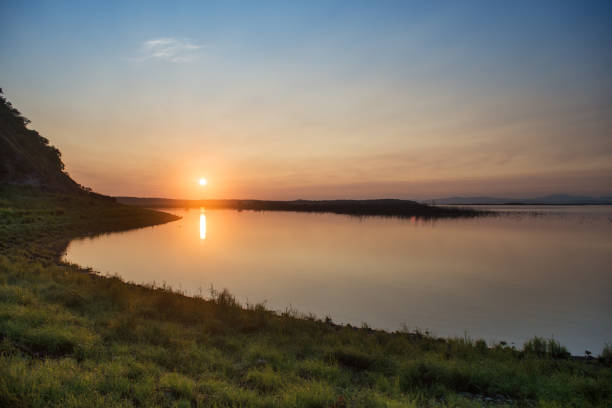 Gorgeous sunset over the River Amur. Beautiful view on a wide stretch of water in the evening. The rays of the setting sun light up the clouds in the sky and illuminate the water. Gleams play on the waves. The Amur River, the largest river in the far East.