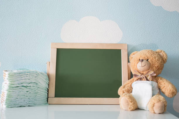 Diapers and blank chalkboard. Teddy bear dressed in diaper. top view. frame with a copy space