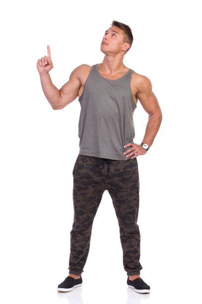 fit man in gray tank top and camo pants looking up and pointing - camouflage pants photos et images de collection