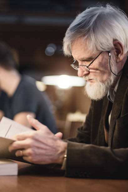 istock Senior Man Sitting in the Library and Reading a Book 643014620