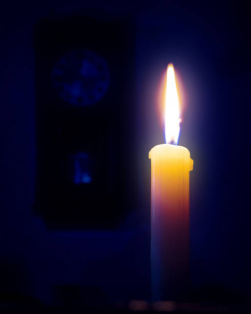 Vintage pendulum clock in dark room lit by single yellow candle with quite flame. Bed time concept.