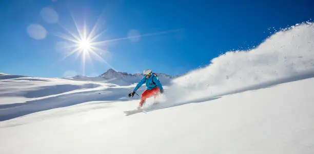 Freerider snowboarder running downhill in beautiful Alpine landscape. Fresh powder snow, blue sky on background.