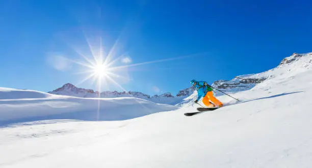 Freerider skier running downhill in beautiful Alpine landscape. Fresh powder snow, blue sky on background.