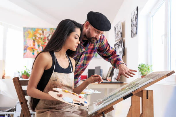 istock Painter overseeing the work of female apprentice 643035296