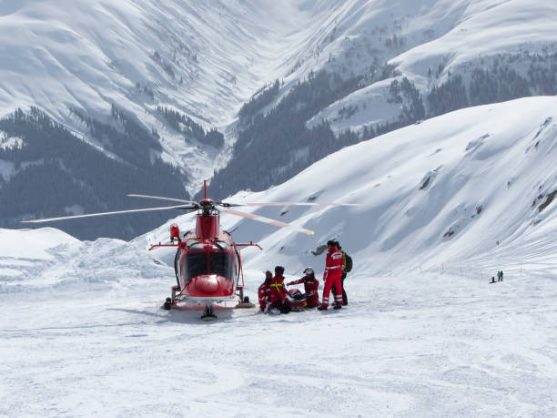 Swiss air rescue helicopter next to injured skier on ski piste Disentis/Muster, Switzerland - 18 February 2014: Next to a landed Agusta A109SP rescue helicopter of Swiss Air-Rescue association "REGA", paramedics provide medical aid to an injured skier on the slope of the ski resort Disentis, Switzerland (Grisons canton). graubunden canton photos stock pictures, royalty-free photos & images