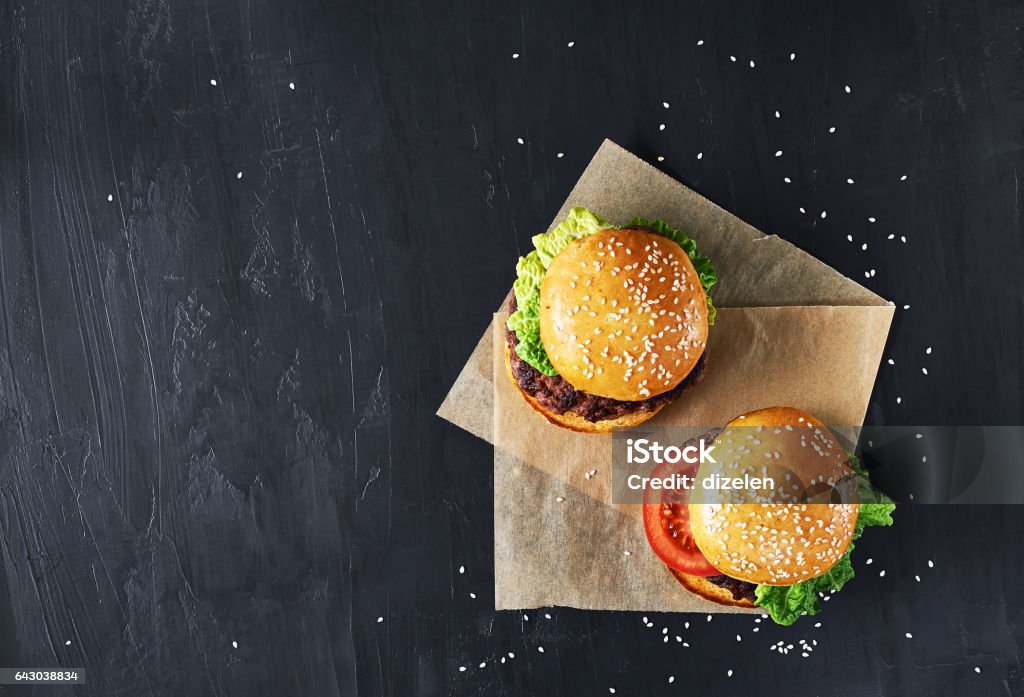 Craft beef burgers with vegetables. Craft beef burgers with vegetables. Flat lay on black textured background with sesame seeds. Burger Stock Photo