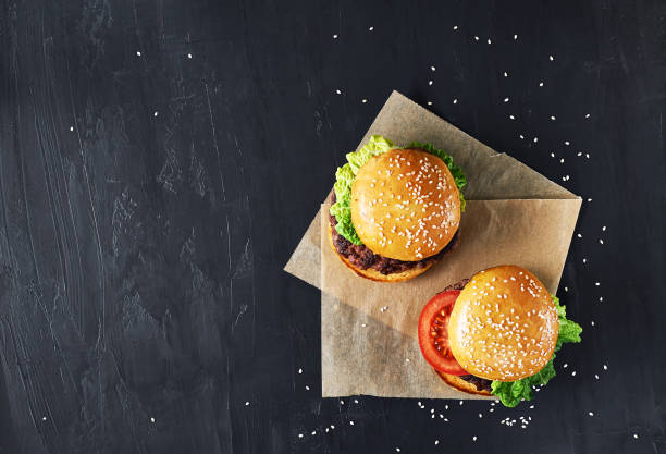 Craft beef burgers with vegetables. Craft beef burgers with vegetables. Flat lay on black textured background with sesame seeds. restaurant table layout stock pictures, royalty-free photos & images