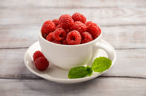 istock Ripe sweet raspberries in white cup on wooden table 643053310