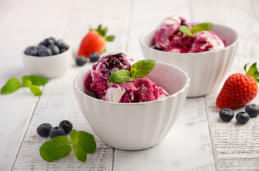 Ice cream with blueberries and strawberries in white bowl on white wooden background, selective focus