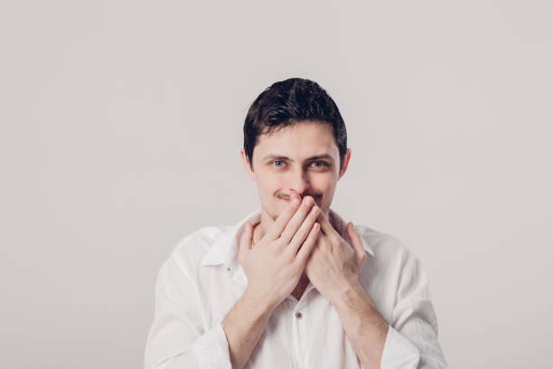 istock young man in white shirt covers his mouth with his hands on gray 643060048