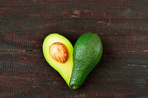 Fresh avocado in the shape of a heart isolated on wood table background. Love symbol made of fruit. Exotic fruit.