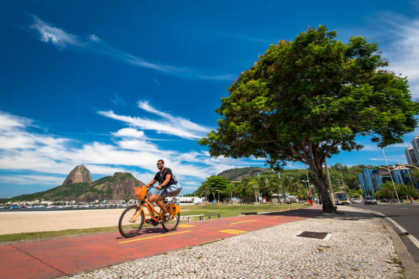 uomo in bicicletta nella spiaggia di botafogo - brazil bicycle rio de janeiro outdoors foto e immagini stock