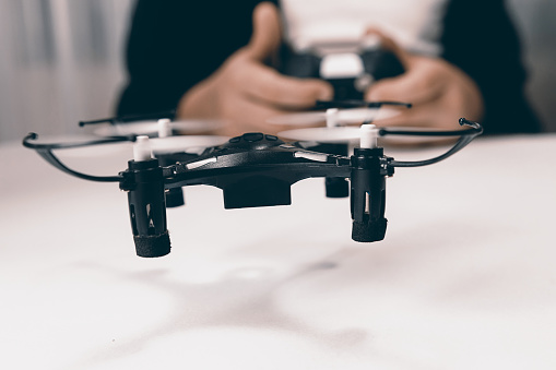 Boy hands with a remote control flying a small drone toy indoors.