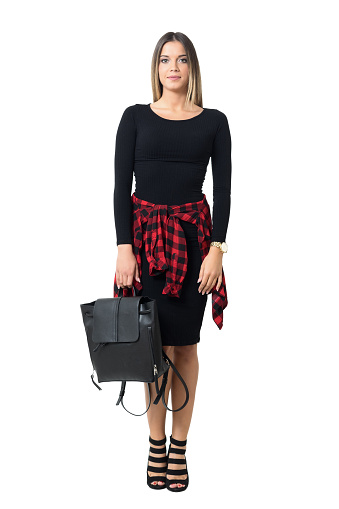 Stylish young woman wearing black dress carrying black leather bag looking at camera. Full body length isolated over white studio background.