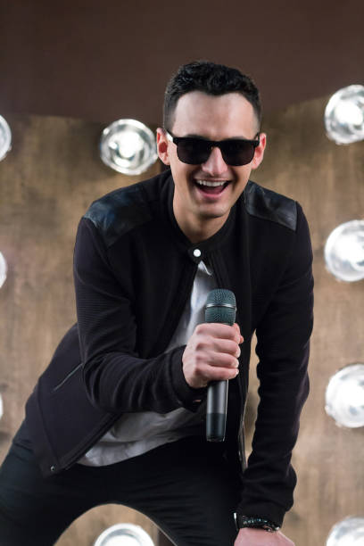 istock Male singer in sunglasses with microphone singing in projectors lights 643134064