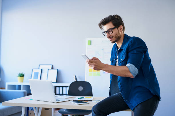 istock Designer sitting on desk in office using his smartphone 643134150