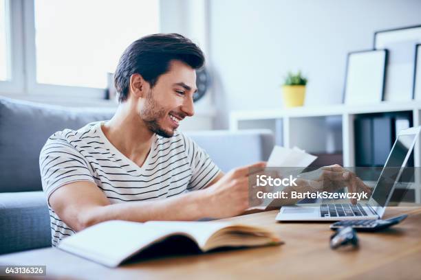 Uomo Felice Che Paga Le Bollette Sul Suo Laptop In Salotto - Fotografie stock e altre immagini di Bolletta