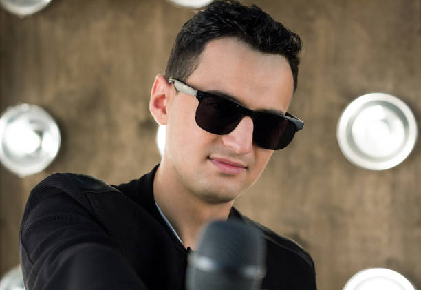 istock Male singer in sunglasses with microphone performs in projectors lights 643136346