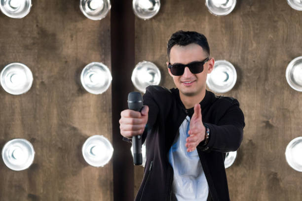 istock Male singer in black with microphone performs in projectors lights 643136404