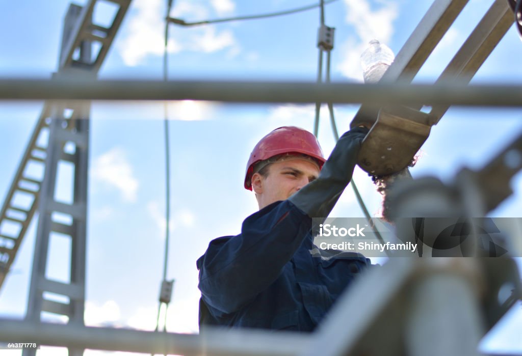 Electrician working in hight with protective equipment Construction worker working in power substation. Power Line Stock Photo