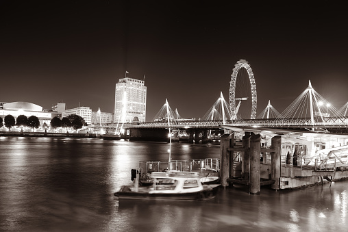 Thames River night view with office buildings, boat and London eye in black and white.
