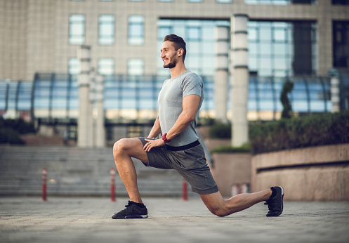 Young athletic man in a lunge position on the street.