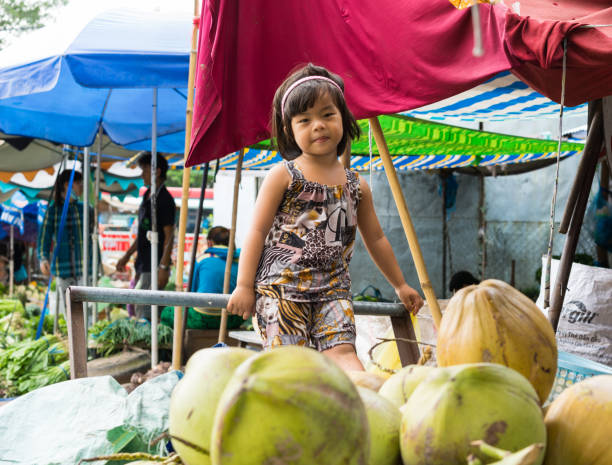 Vinh Long, Vietnam - Nov 30, 2014: Unidentified child plays alone among a lot of fruits at Vinh Long market, Mekong delta. Almost local people at market are poverty Vinh Long, Vietnam - Nov 30, 2014: Unidentified child plays alone among a lot of fruits at Vinh Long market, Mekong delta. Almost local people at market are poverty vietnamese girls for sale stock pictures, royalty-free photos & images