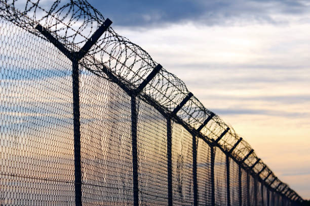 silhouette of barbed wire fence against a cloudy sky - sinais de cruzamento imagens e fotografias de stock
