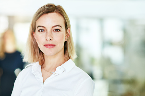 Portrait of an ambitious young woman standing in a modern office with her colleagues in the background